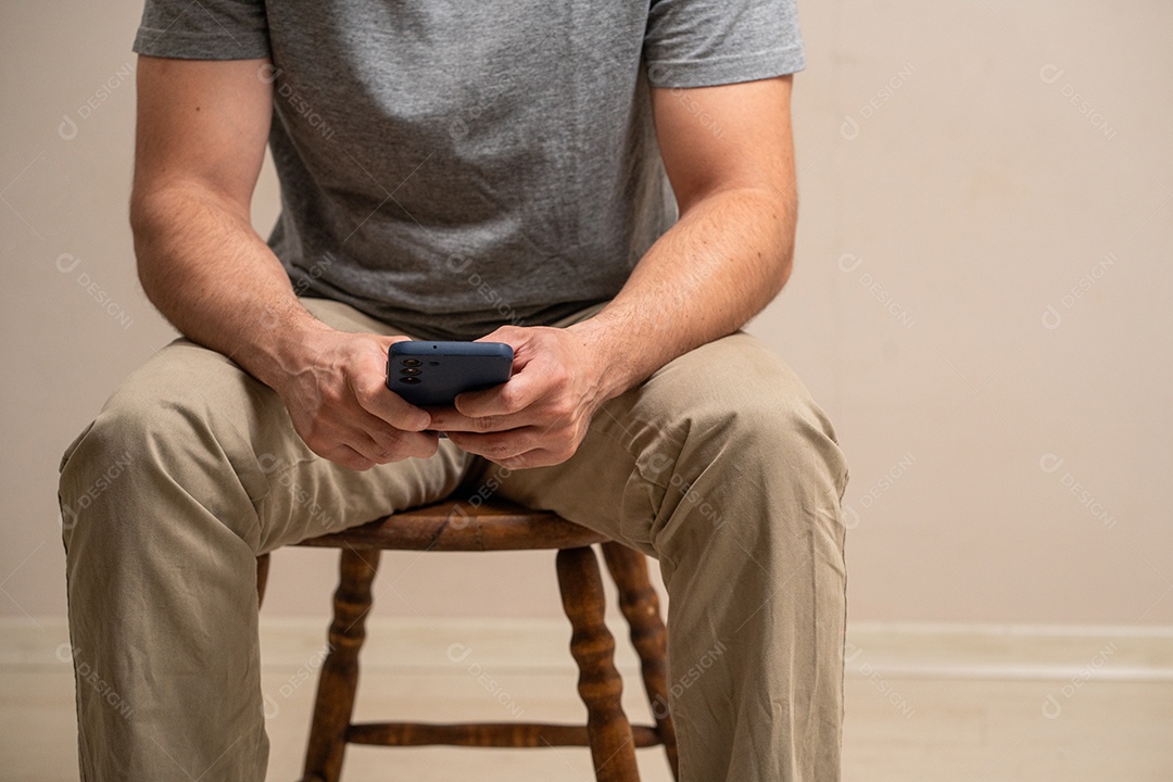 Homem sentado segurando um smartphone em fundo pastel.