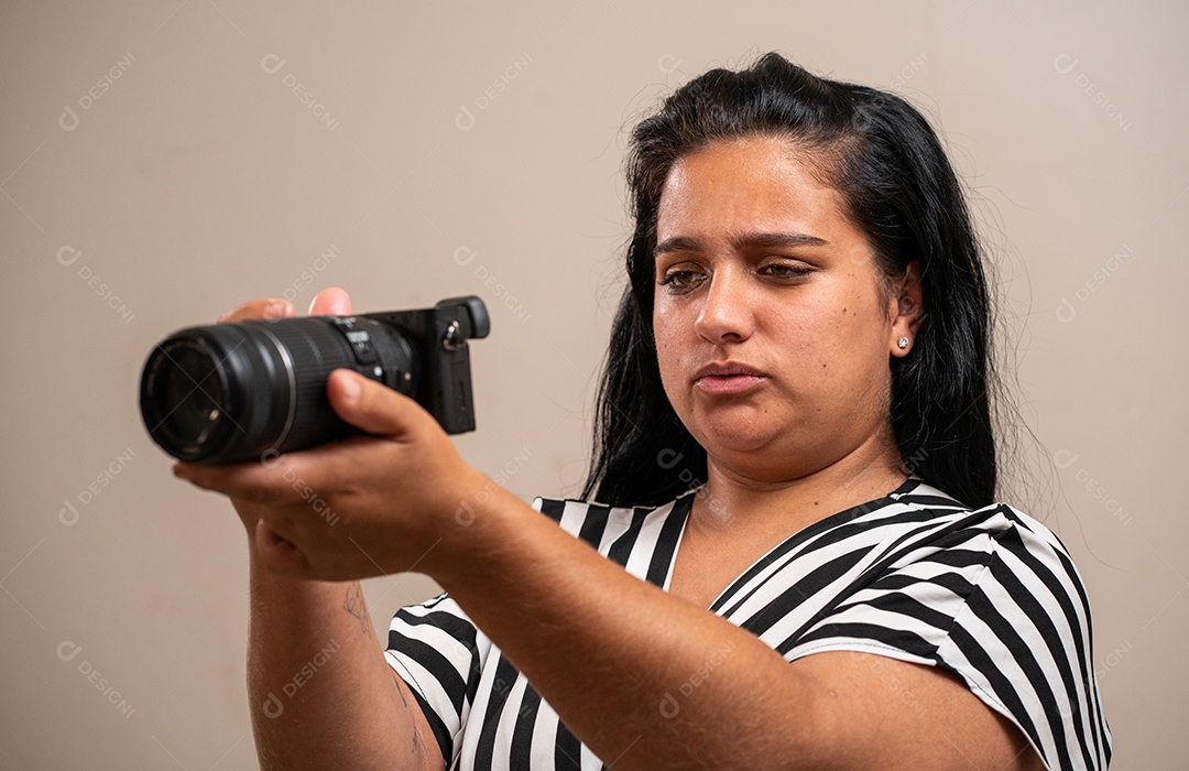 Jovem morena segurando uma câmera em fundo pastel.