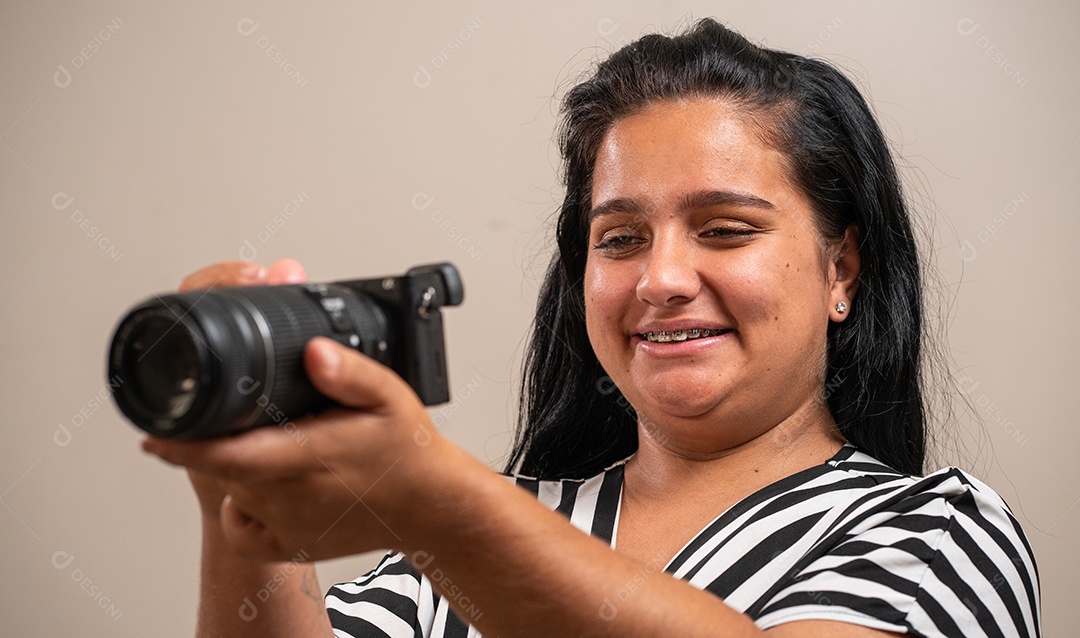Jovem morena segurando uma câmera em fundo pastel.