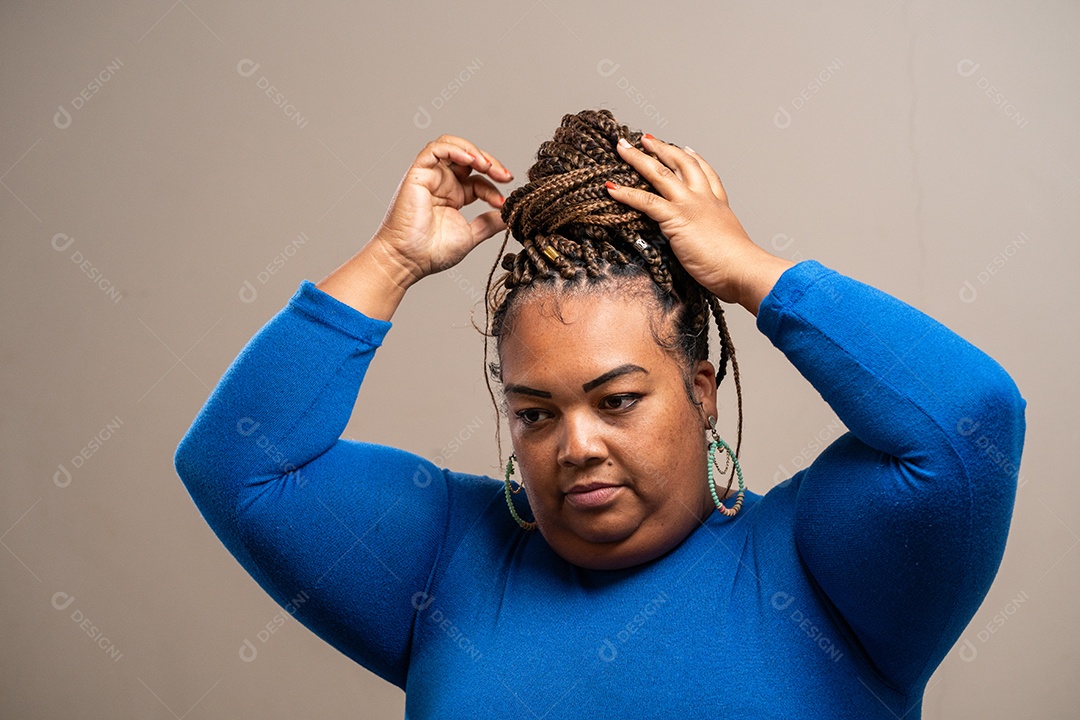 Jovem com tranças afro amarrando o cabelo em fundo pastel.