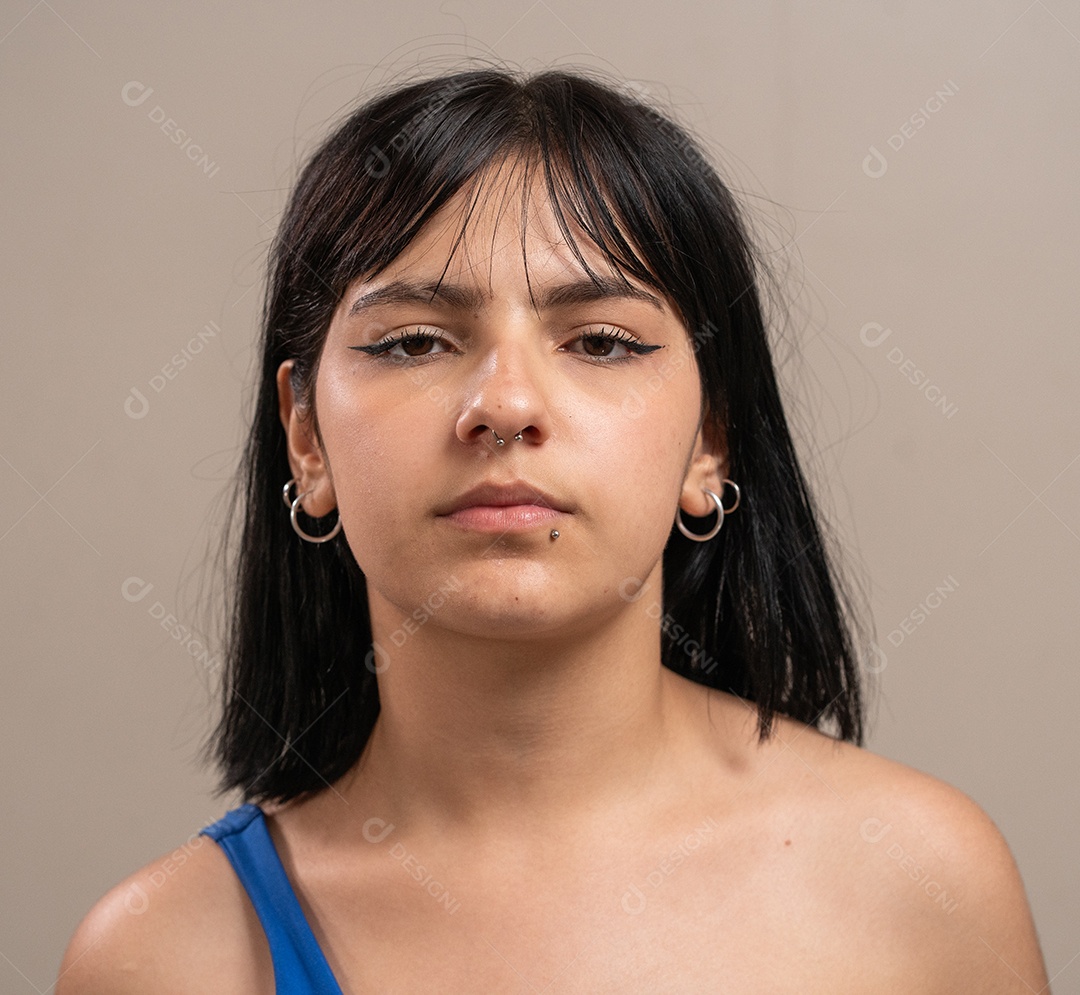 Menina com piercings faciais olhando para a câmera com expressão neutra em fundo pastel.