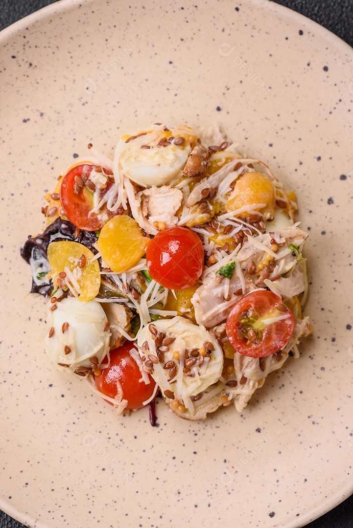 Deliciosa salada fresca com frango, ovos de codorna, tomate cereja, alface, sal e especiarias sobre fundo escuro de concreto