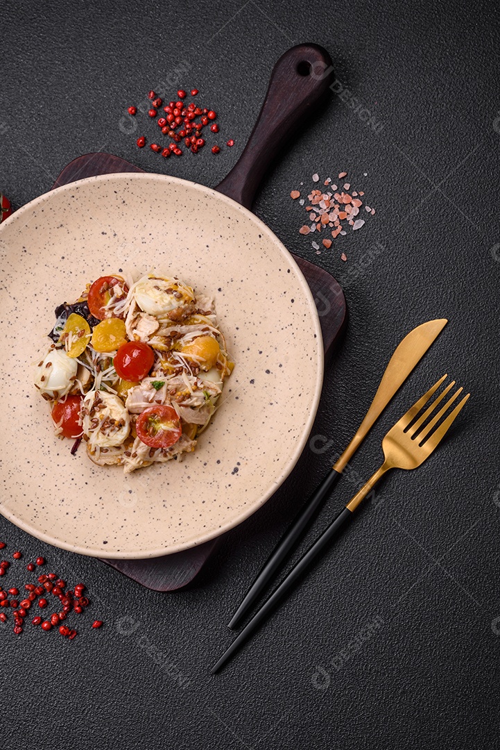 Deliciosa salada fresca com frango, ovos de codorna, tomate cereja, alface, sal e especiarias sobre fundo escuro de concreto
