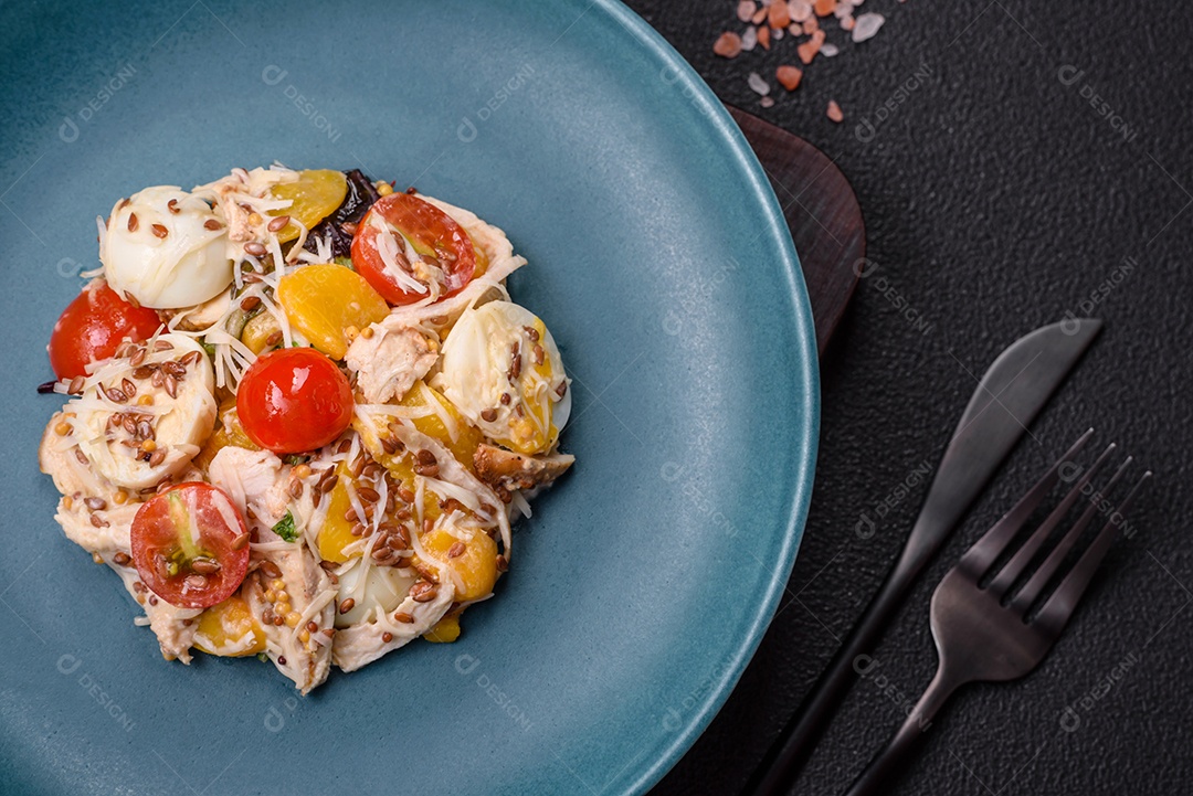 Deliciosa salada fresca com frango, ovos de codorna, tomate cereja, alface, sal e especiarias sobre fundo escuro de concreto