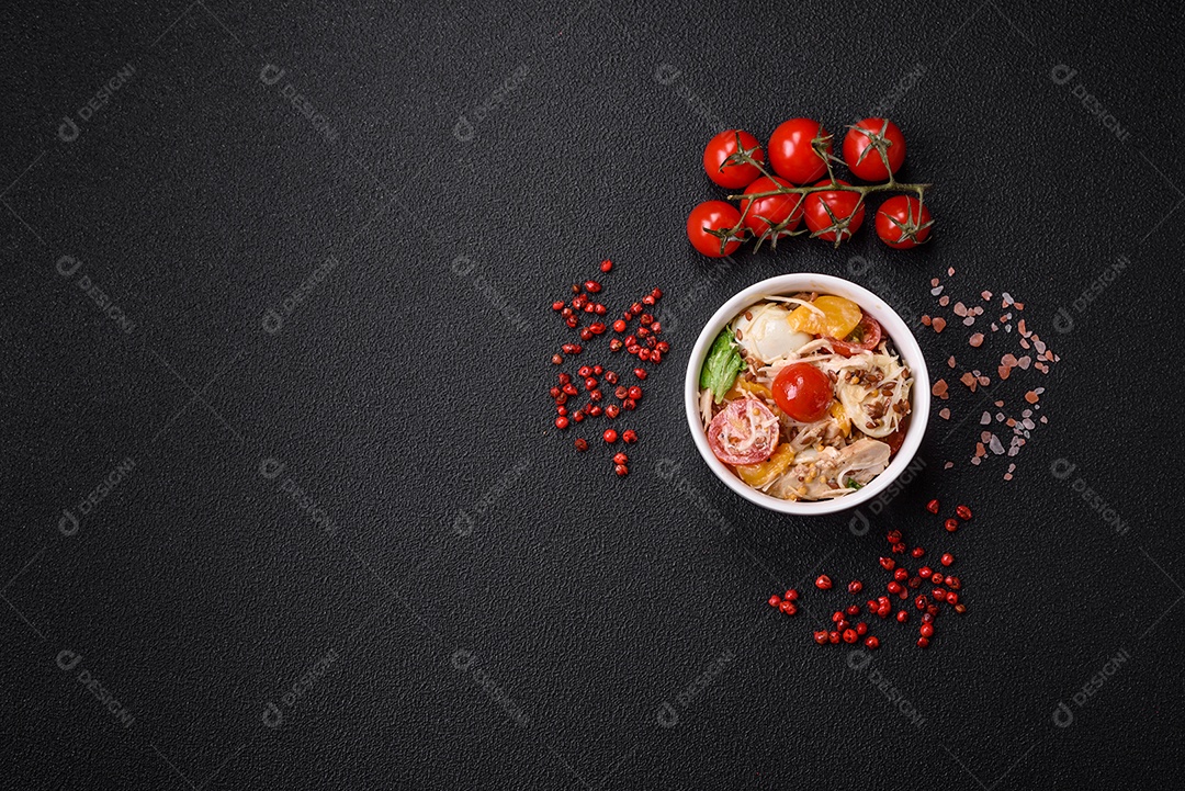 Deliciosa salada fresca com frango, ovos de codorna, tomate cereja, alface, sal e especiarias sobre fundo escuro de concreto