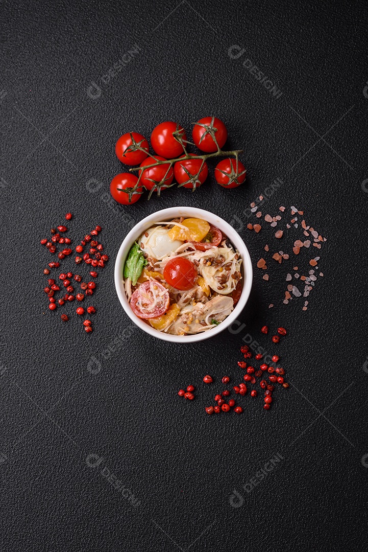 Deliciosa salada fresca com frango, ovos de codorna, tomate cereja, alface, sal e especiarias sobre fundo escuro de concreto
