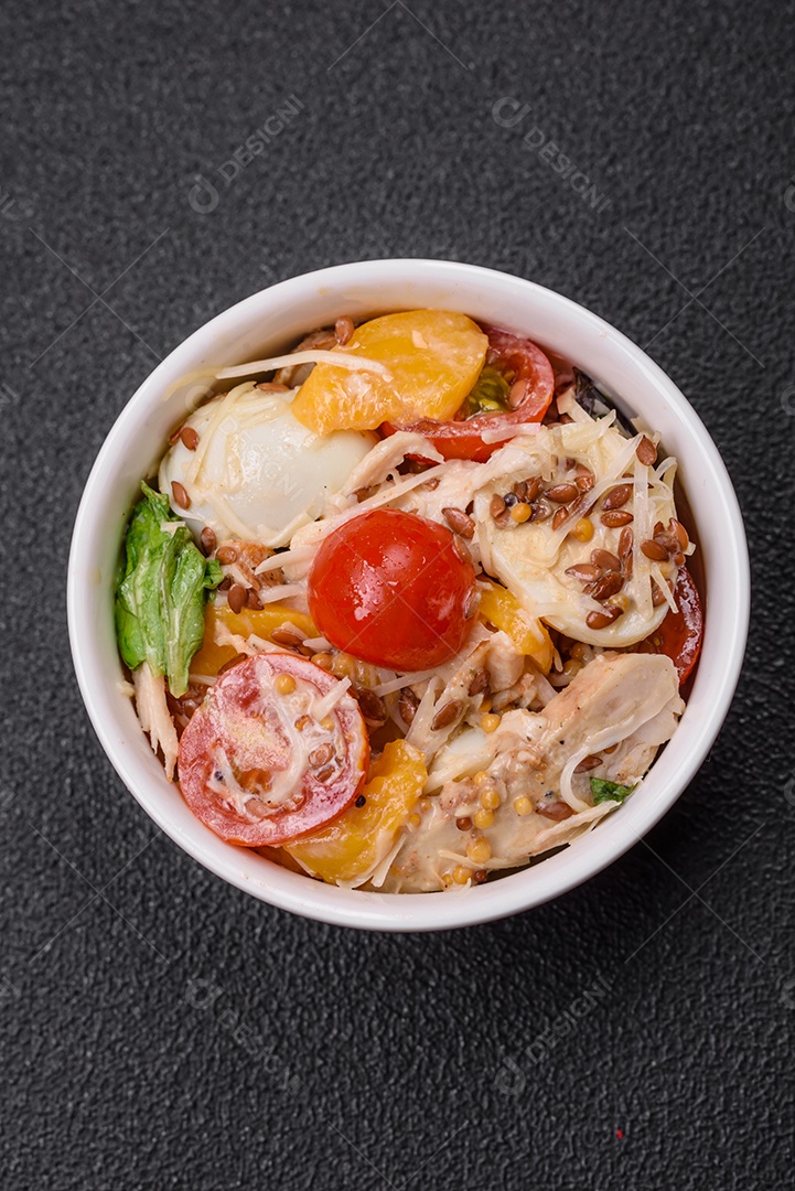 Deliciosa salada fresca com frango, ovos de codorna, tomate cereja, alface, sal e especiarias sobre fundo escuro de concreto