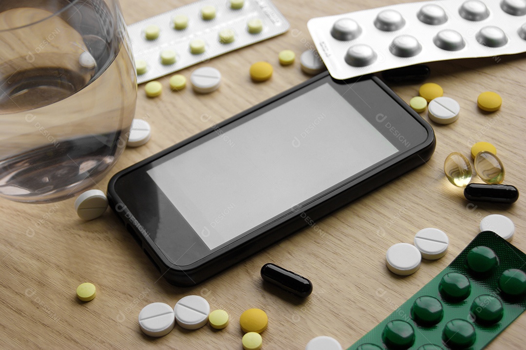 Comprimidos e capsulas copo de água e uma celular sobre mesa de madeira