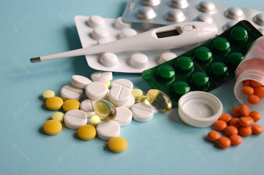 Diversos comprimidos e cartelas de remédio com termômetro sobre fundo azul