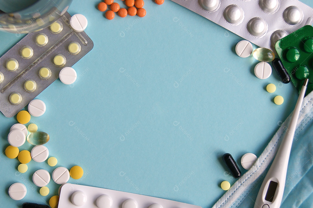 Diversos comprimidos e cartelas de remédio com termômetro sobre fundo azul