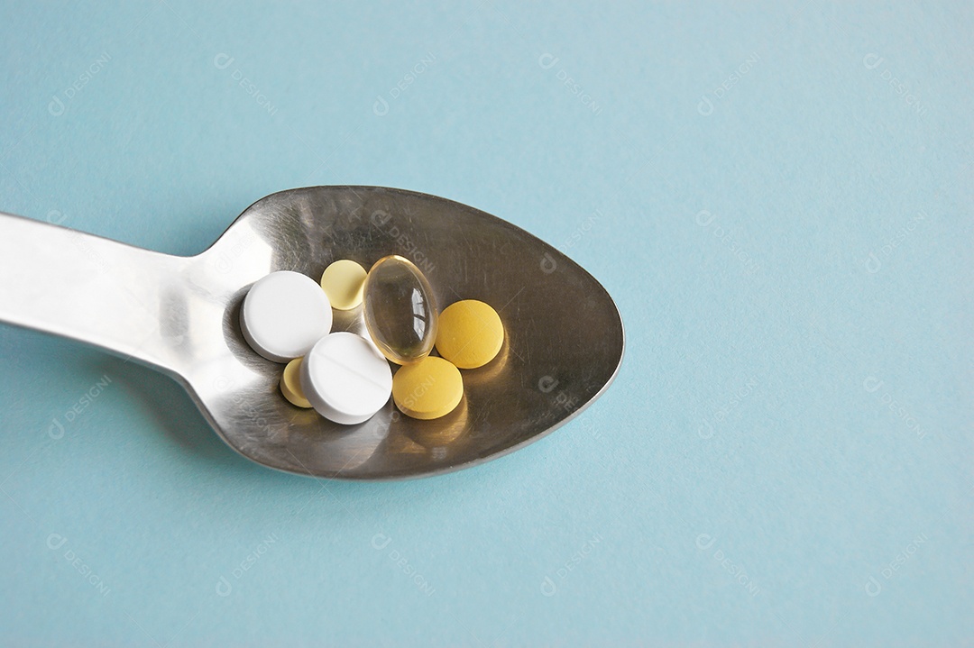 Comprimidos variados de medicamentos, comprimidos e cápsulas numa colher de metal