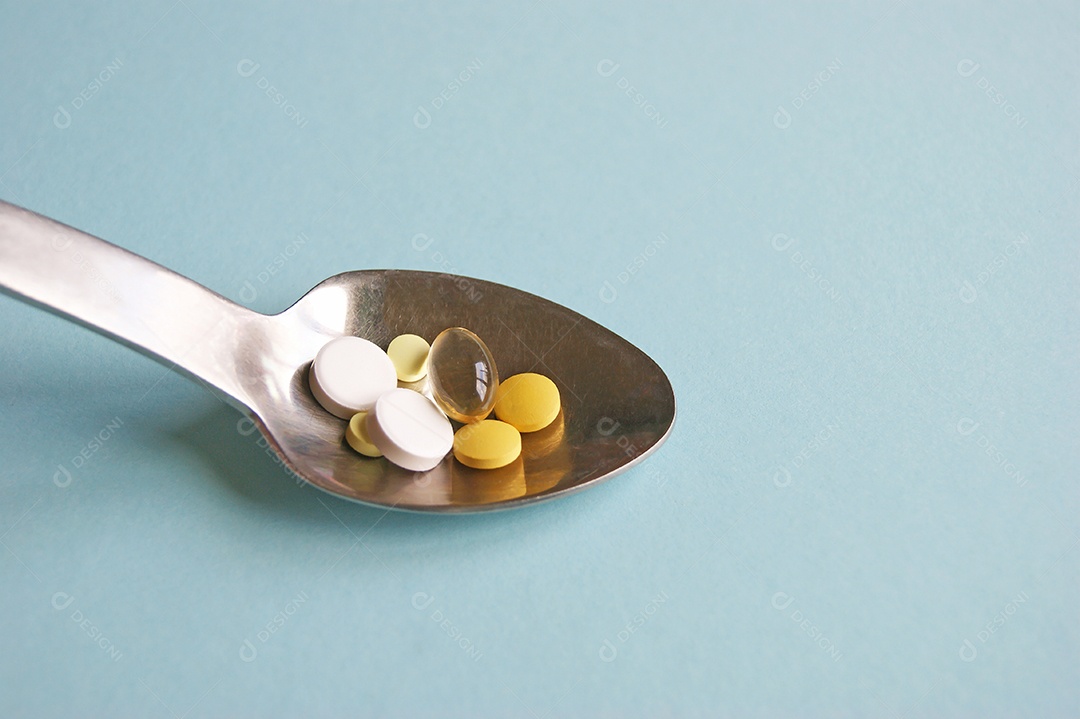 Comprimidos variados de medicamentos, comprimidos e cápsulas numa colher de metal