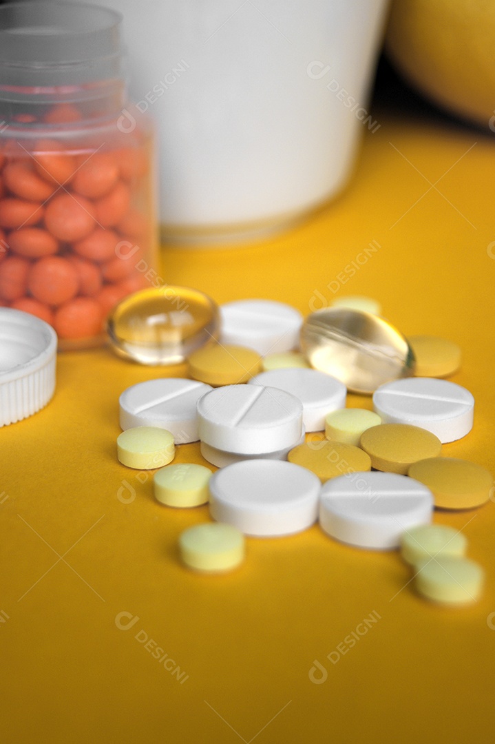 Diversos comprimidos, comprimidos e cápsulas de medicamentos farmacêuticos em fundo amarelo.