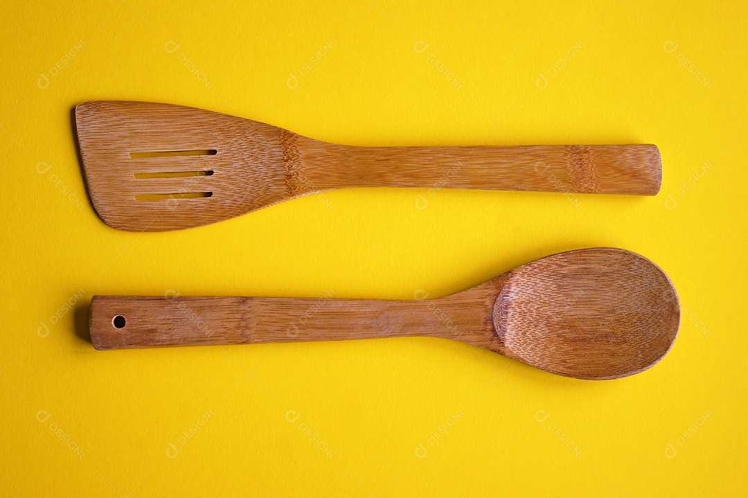 A colher de cozinha de madeira e a espátula isoladas em fundo amarelo