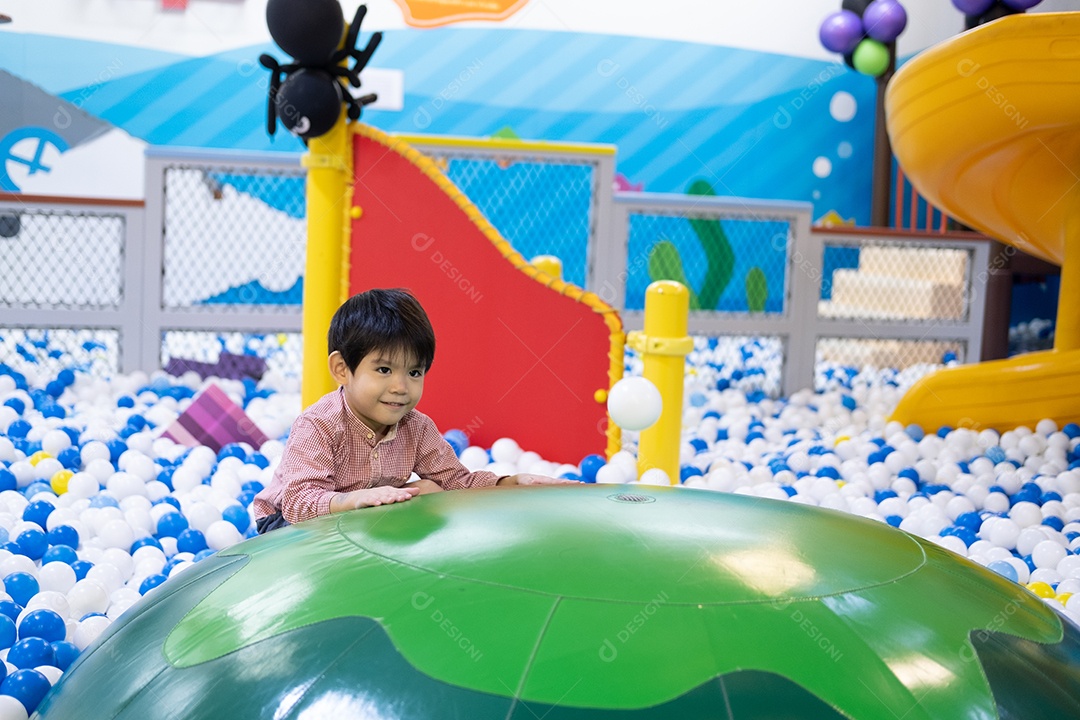Menino asiático olhando para uma bola flutuante entre muitas bolas pequenas