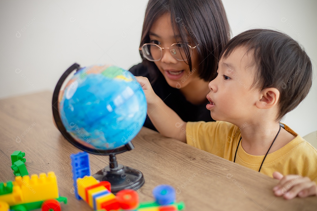 Irmão e irmã asiáticos brincam com um designer de blocos de brinquedo na mesa da sala de estar em casa.