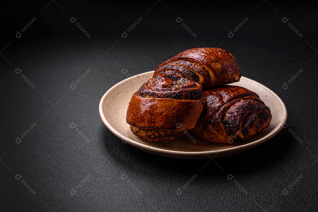 Deliciosos pães doces assados ​​com sementes de papoula e canela em uma placa de cerâmica sobre um fundo escuro de concreto