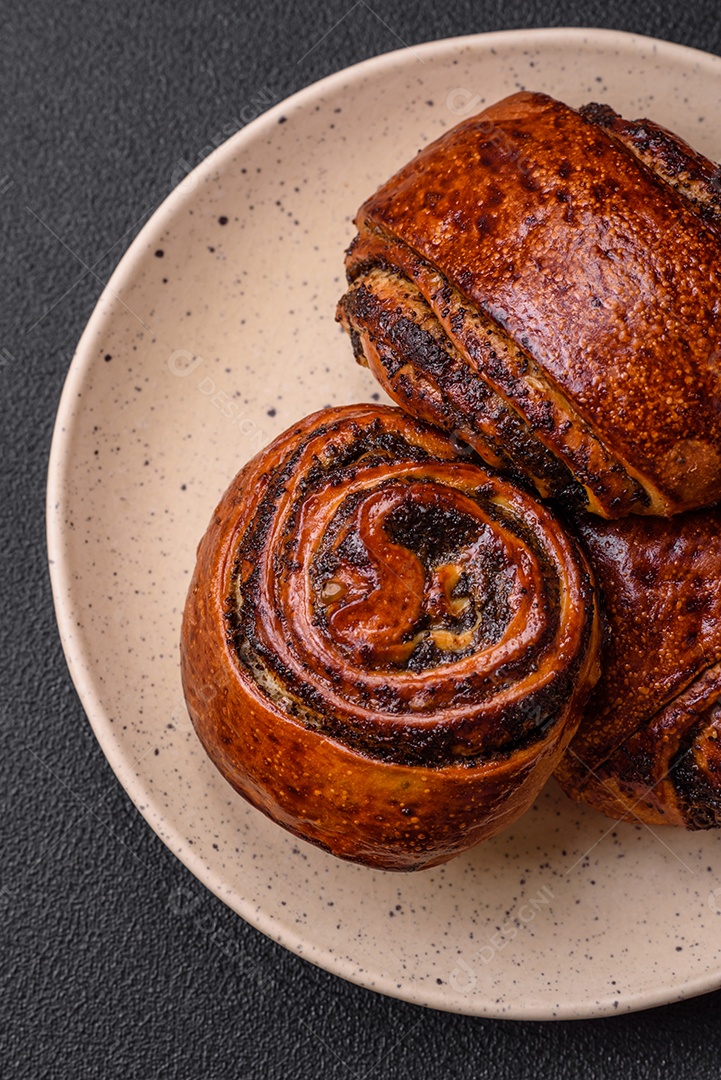 Deliciosos pães doces assados ​​com sementes de papoula e canela em uma placa de cerâmica sobre um fundo escuro de concreto
