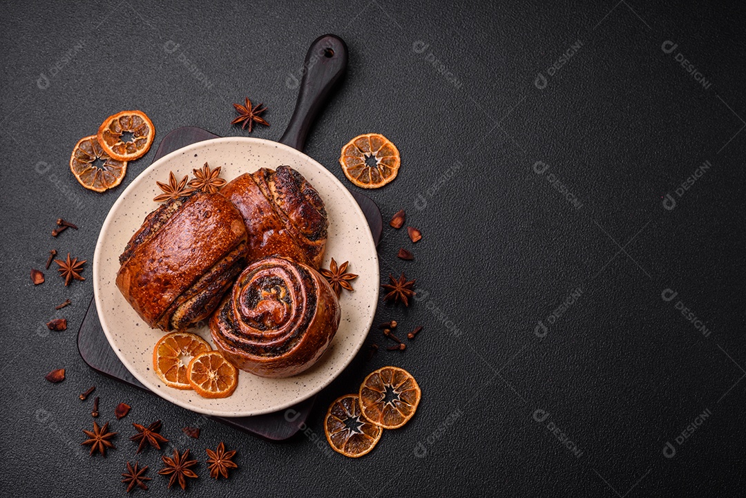 Deliciosos pães doces assados ​​com sementes de papoula e canela em uma placa de cerâmica sobre um fundo escuro de concreto