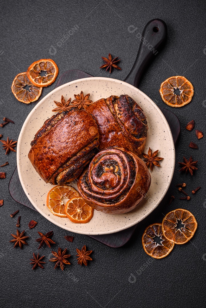 Deliciosos pães doces assados ​​com sementes de papoula e canela em uma placa de cerâmica sobre um fundo escuro de concreto