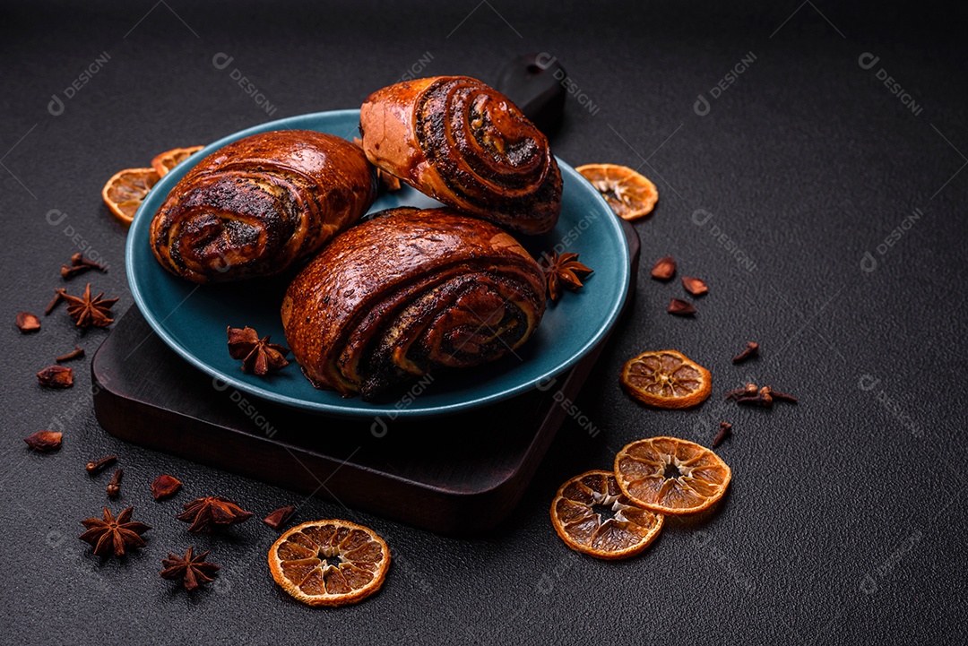 Deliciosos pães doces assados ​​com sementes de papoula e canela em uma placa de cerâmica sobre um fundo escuro de concreto