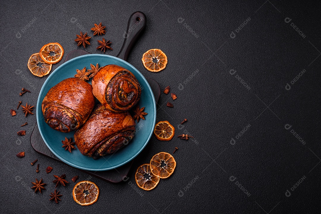 Deliciosos pães doces assados ​​com sementes de papoula e canela em uma placa de cerâmica sobre um fundo escuro de concreto