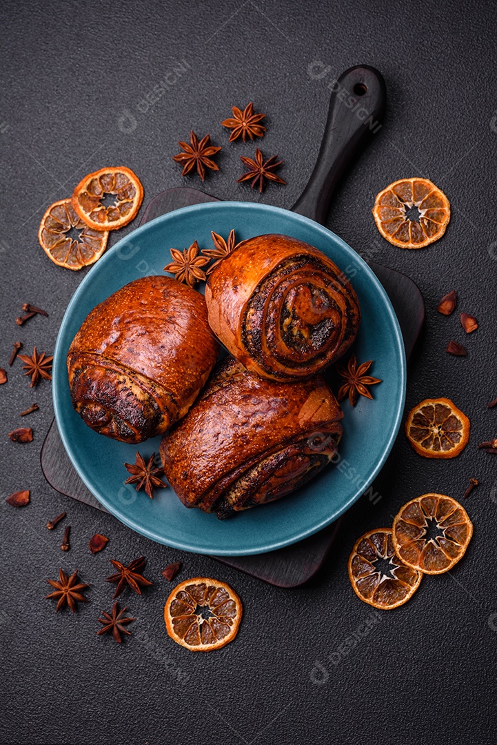 Deliciosos pães doces assados ​​com sementes de papoula e canela em uma placa de cerâmica sobre um fundo escuro de concreto