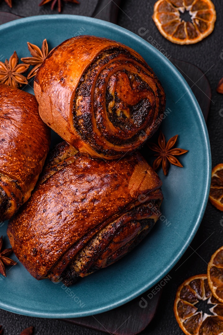 Deliciosos pães doces assados ​​com sementes de papoula e canela em uma placa de cerâmica sobre um fundo escuro de concreto