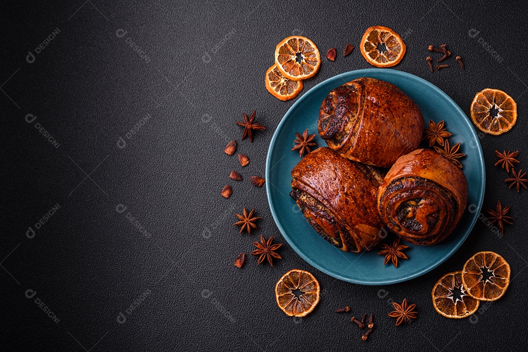 Deliciosos pães doces assados ​​com sementes de papoula e canela em uma placa de cerâmica sobre um fundo escuro de concreto