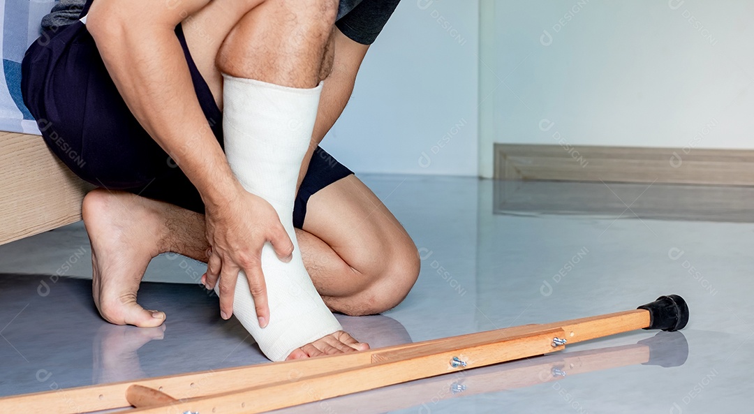 Triste homem asiático deprimido sofrendo perto da cama, ele está sentado e tocando-o e estressado com sintomas de uma perna quebrada e um gesso branco