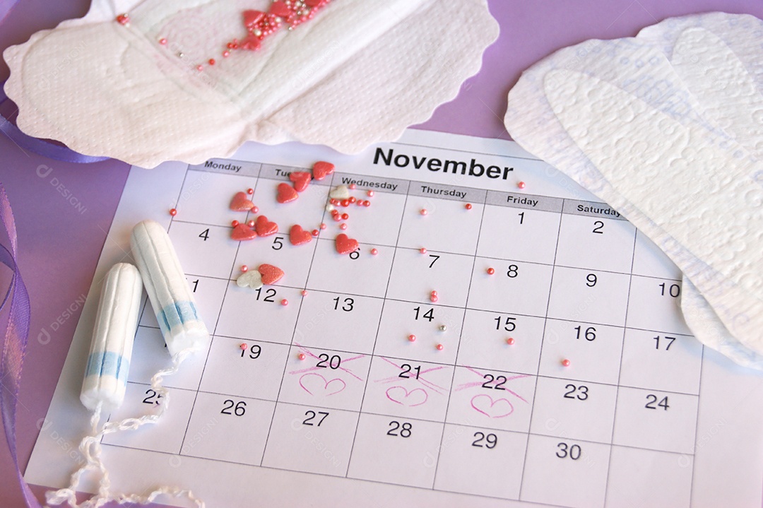 Os absorventes menstruais e tampões no calendário do período menstrual com fundo lilás.