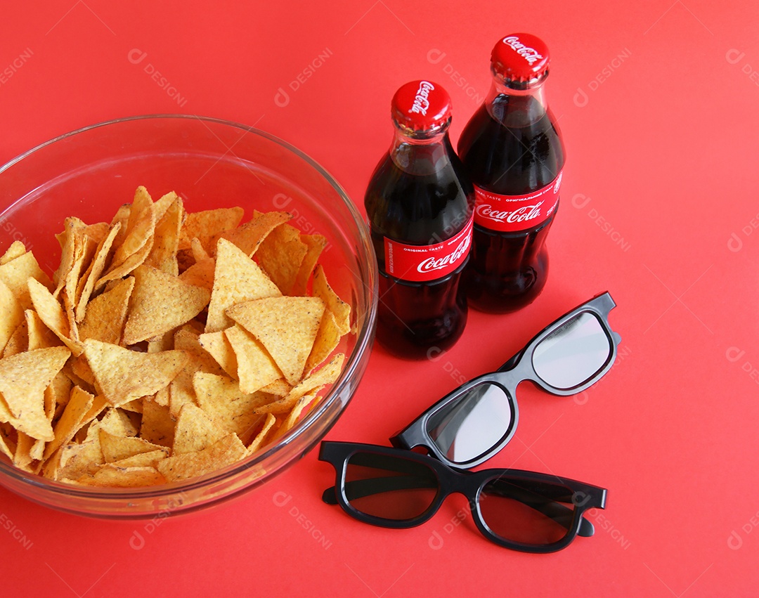 Nachos em tigela e coca cola gelada com dois óculos em fundo vermelho