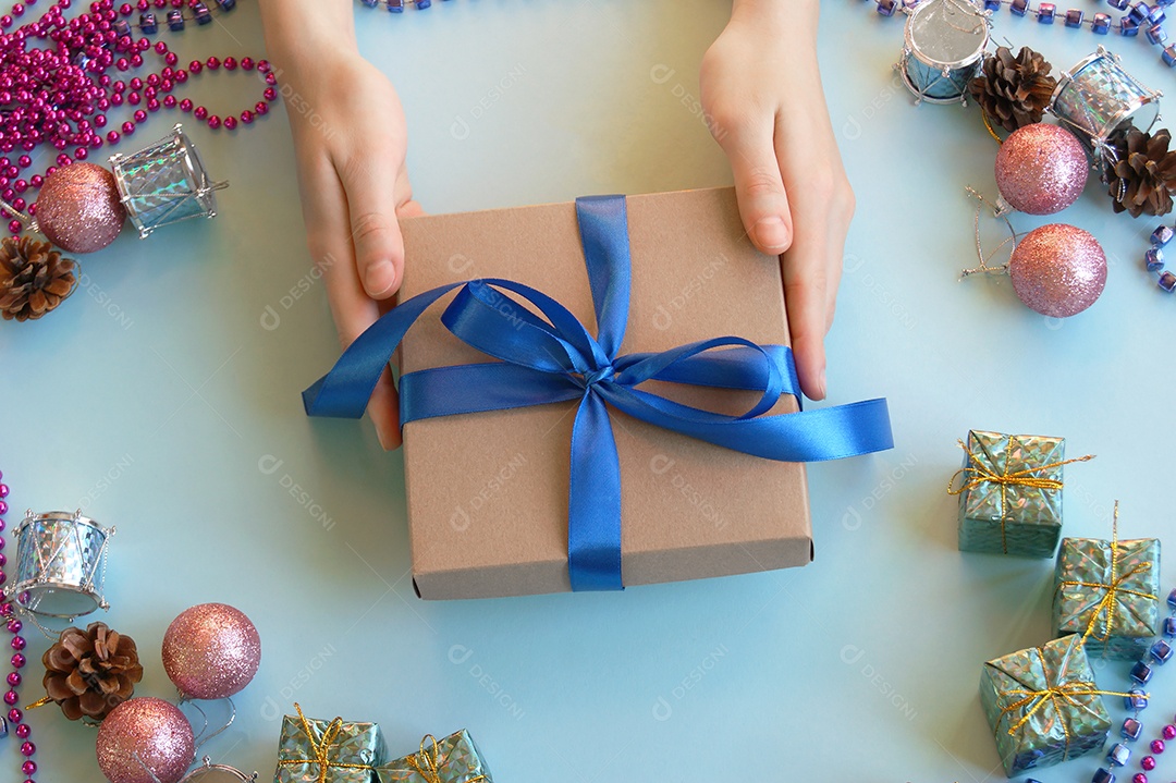 Mão passando fita na caixa de presente com decoração de natal ao fundo