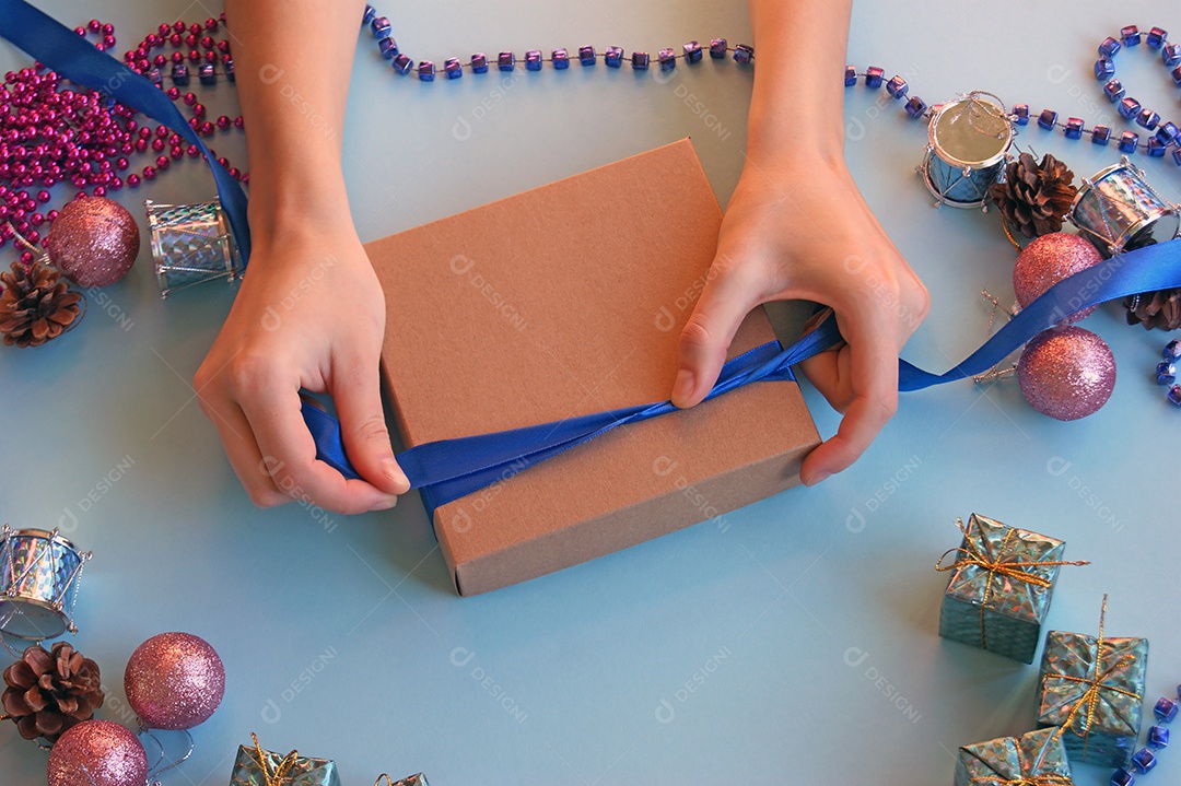 Caixa de presente sendo enrolada com decoração de natal ao fundo
