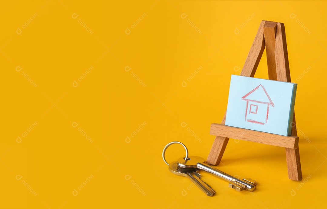 Desenho de uma casa em cima de cavalete de madeira e chaves de lado sobre fundo amarelo