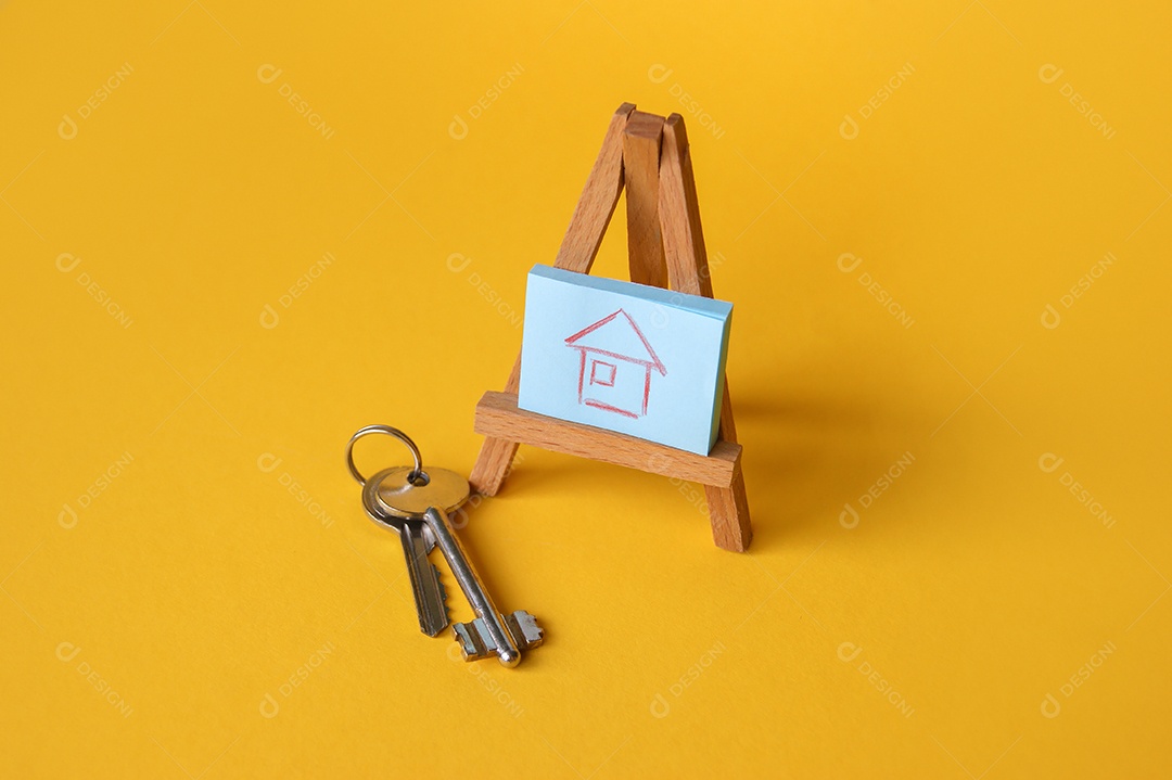 Desenho de uma casa em cima de cavalete de madeira e chaves de lado sobre fundo amarelo