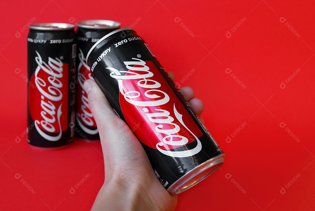 Mão segurando coca cola light e mais duas latas sobre fundo vermelho