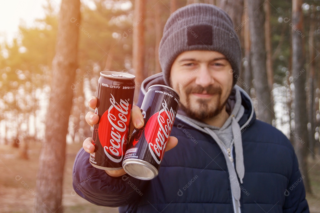 Homem bonito segurando duas coca-cola sobre fundo de natureza