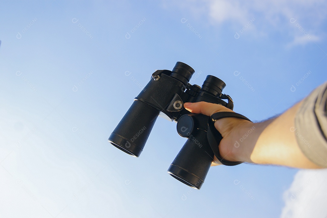 Mão masculina segurando binoculo com fundo de céu azul