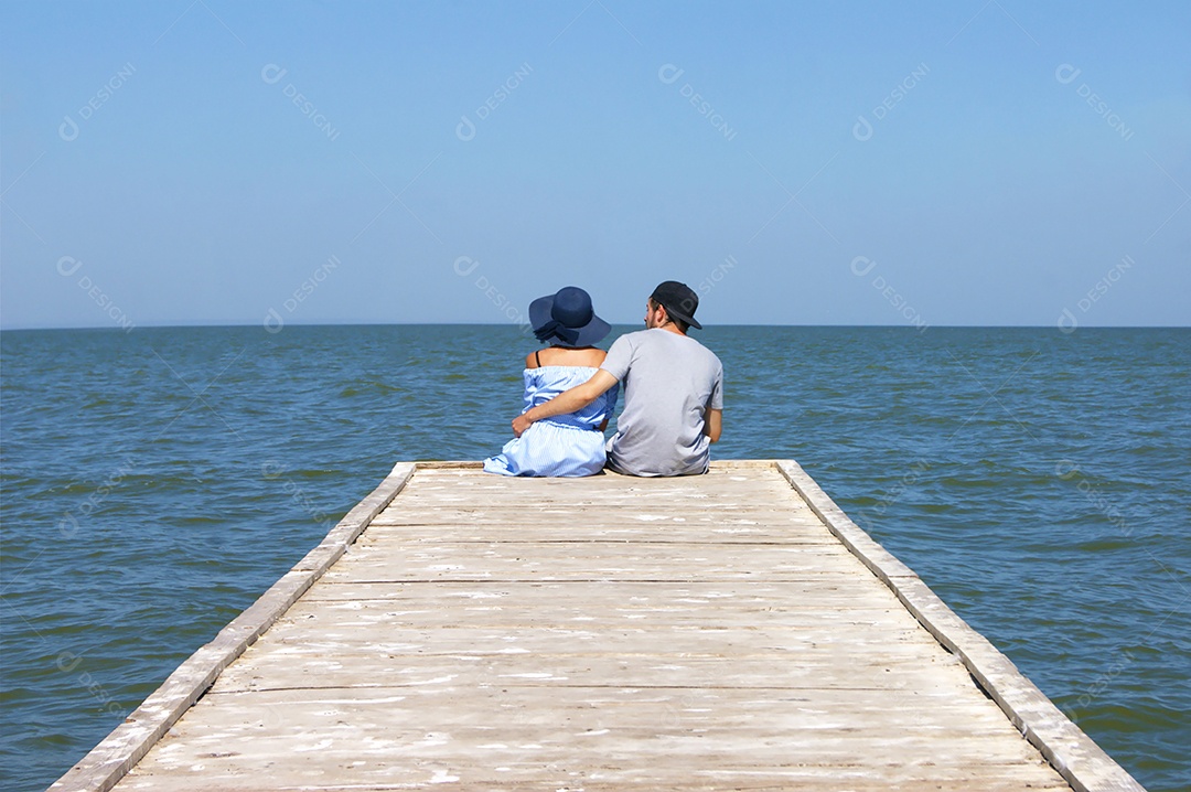 Casal apaixonado sentado na ponta de uma passarela sobre o rio