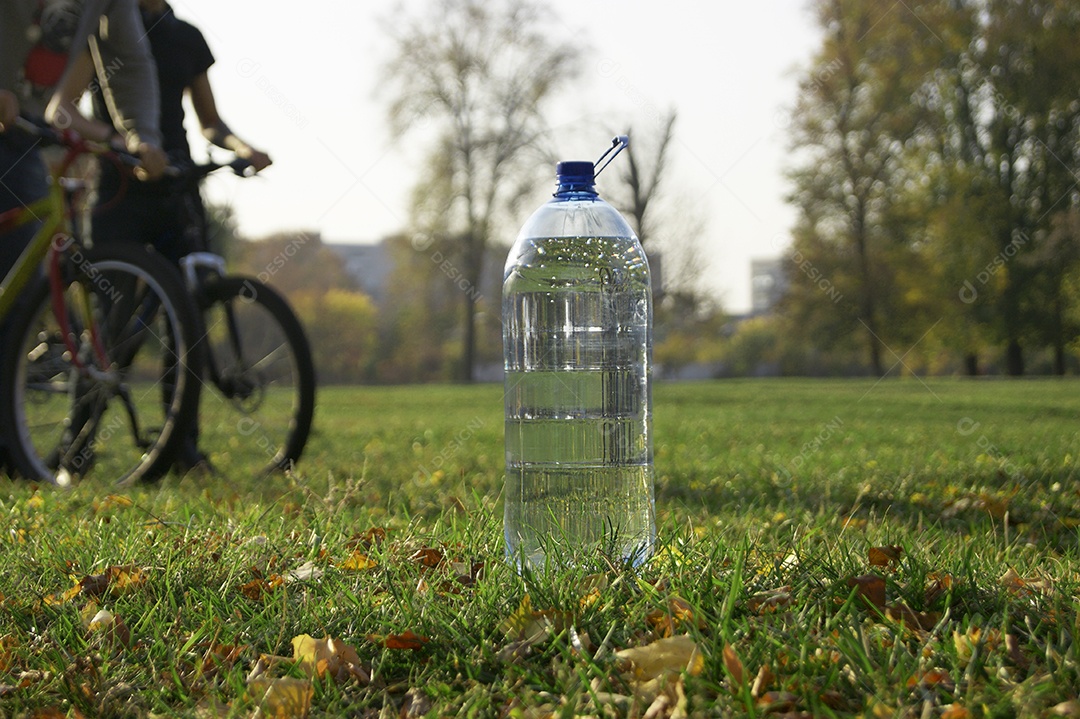 A garrafa de água no parque e dois ciclista de fundo