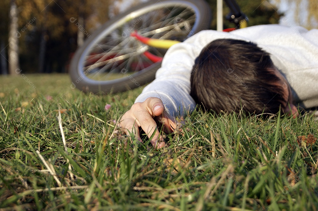 Jovem cai de bicicleta no parque gramado