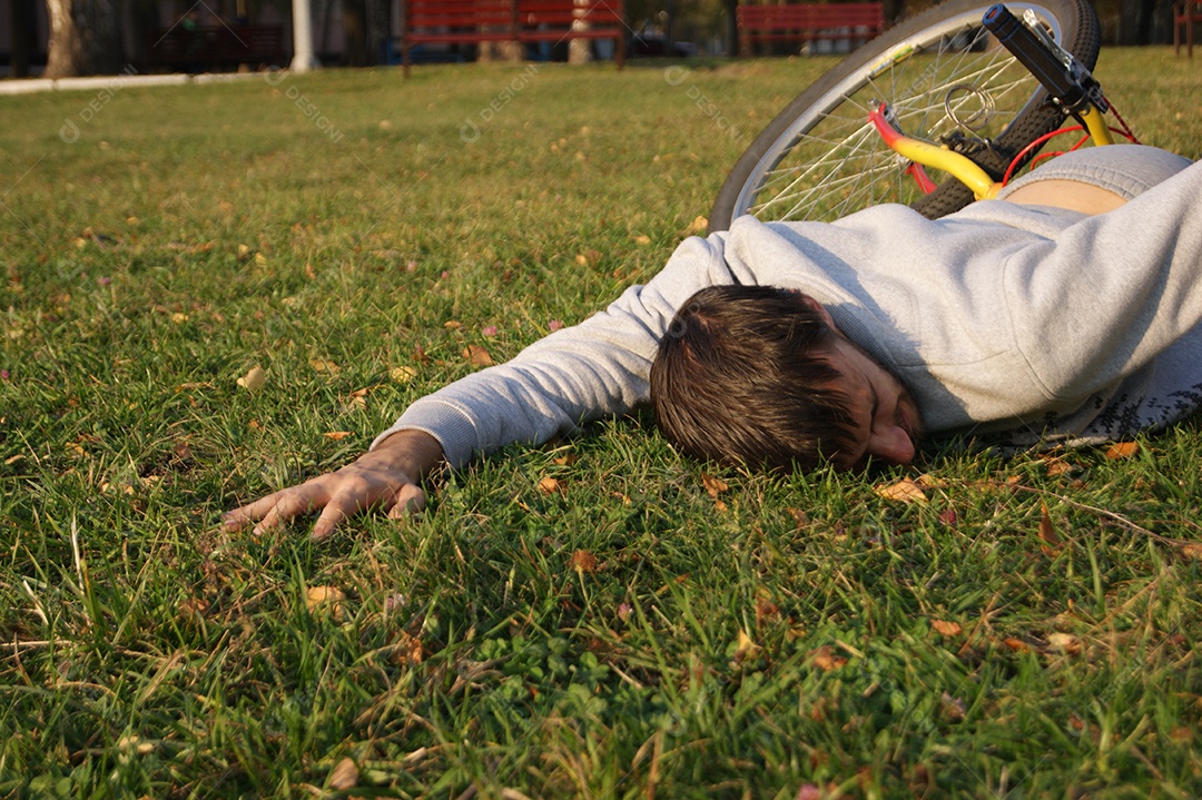 Jovem cai de bicicleta no parque gramado