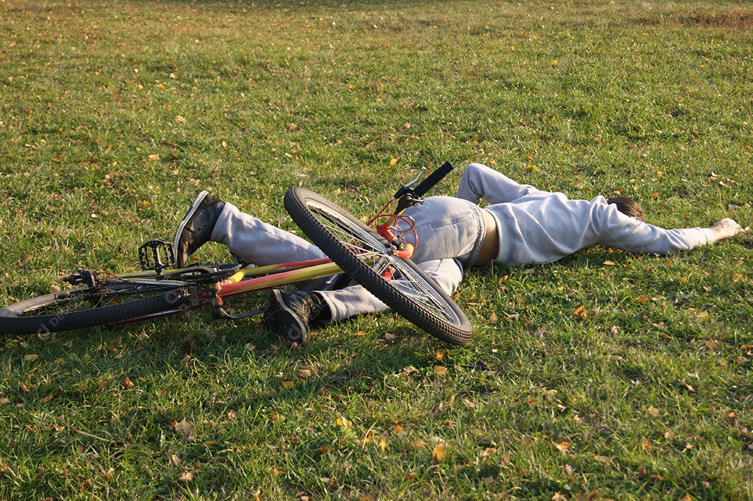Jovem cai de bicicleta no parque gramado