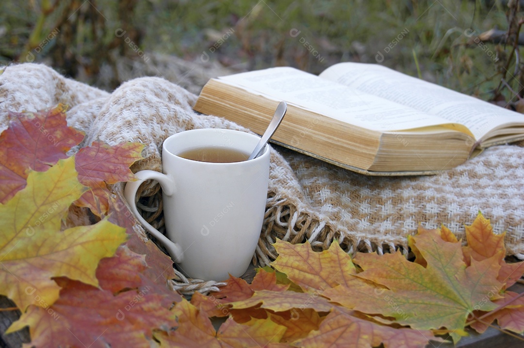 Pano com livro em cima e xícara de chá com colher ao lado