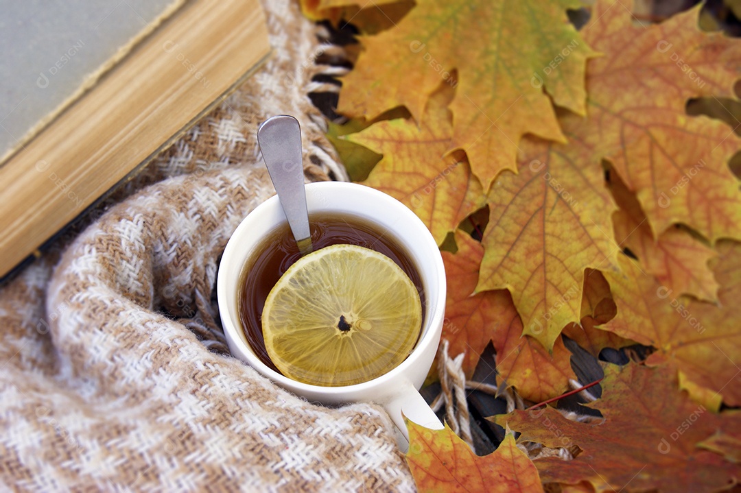 Xícara de chá quente e um livro e folhas caídas sobre o pano de fundo