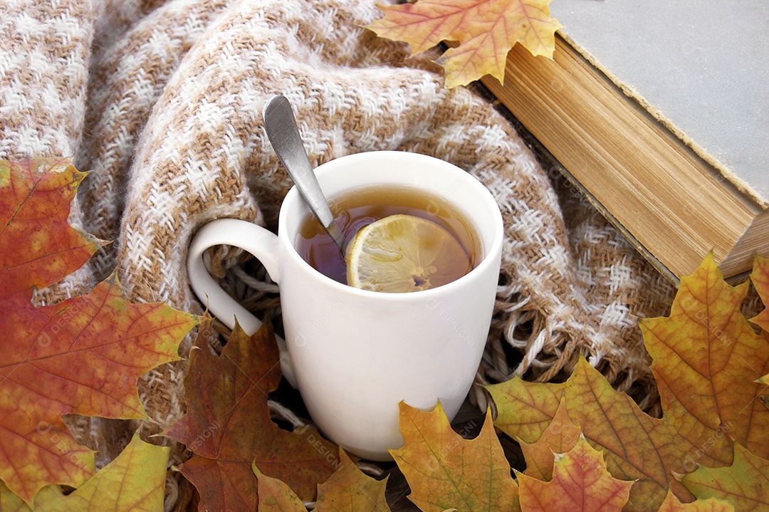 Xícara de chá quente e um livro e folhas caídas sobre o pano de fundo