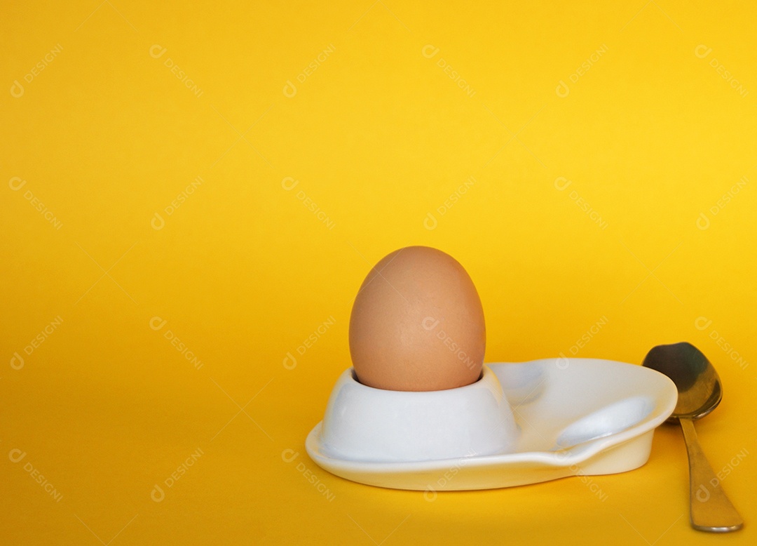 Ovo de galinha e colher ao lado sobre fundo amarelo