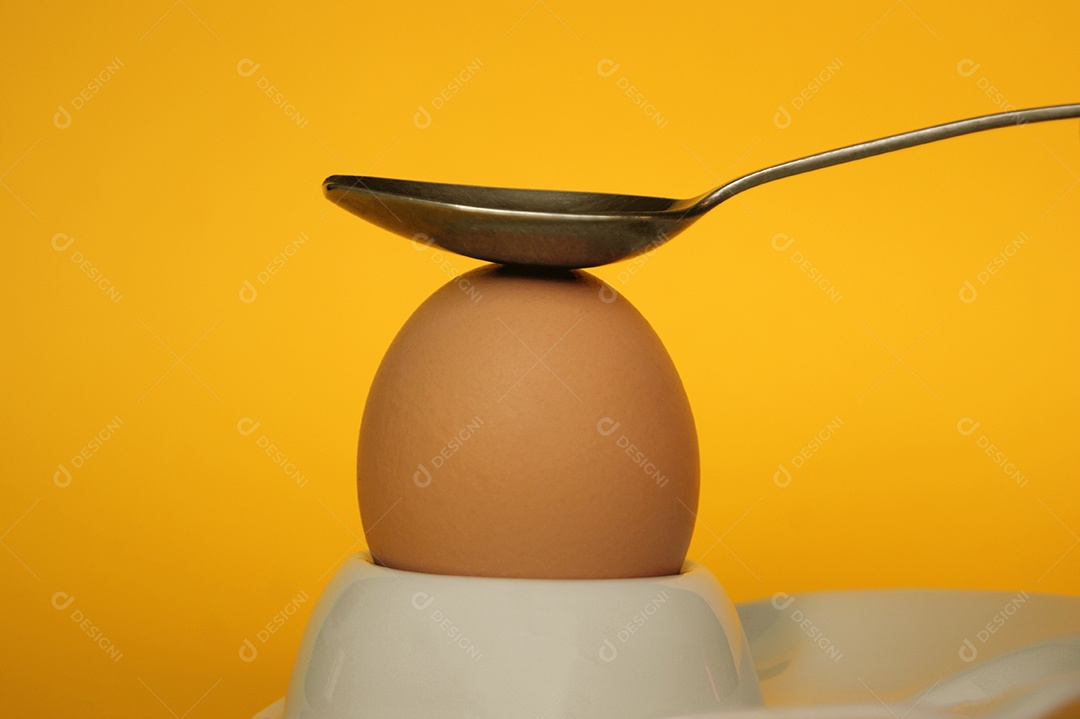 Ovo com colher em cima sobre fundo amarelo