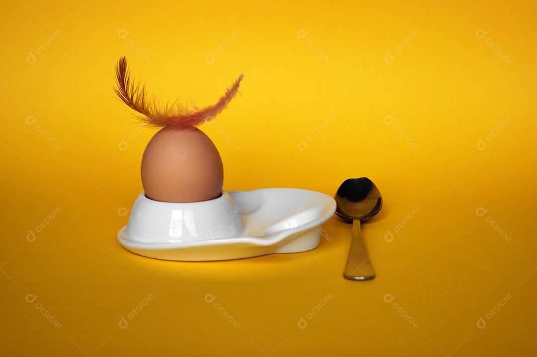 Ovo de galinha com pena em cima e colher ao lado sobre fundo isolado amarelo